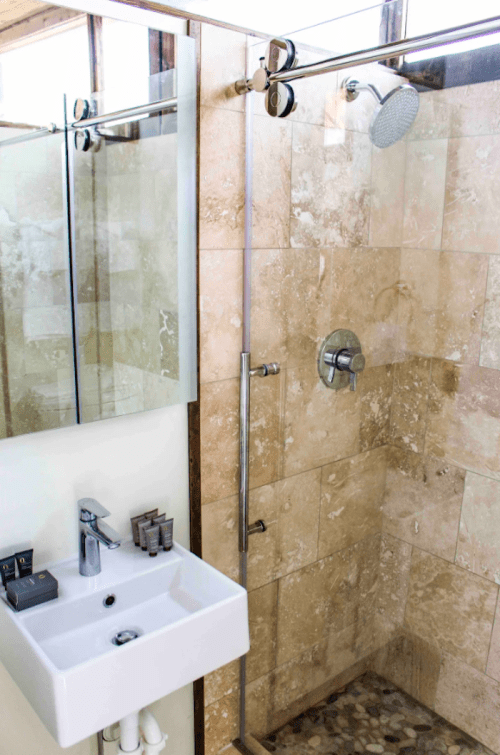 Modern bathroom featuring a glass shower, stone tiles, and a sleek sink with toiletries on the counter.